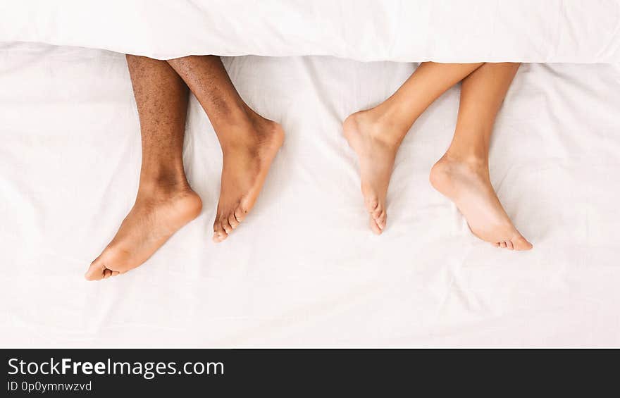 Relationship problems. Conceptual photo of upset couple ignoring each other. Male and female legs under duvet lying on bed, top view, panorama. Relationship problems. Conceptual photo of upset couple ignoring each other. Male and female legs under duvet lying on bed, top view, panorama