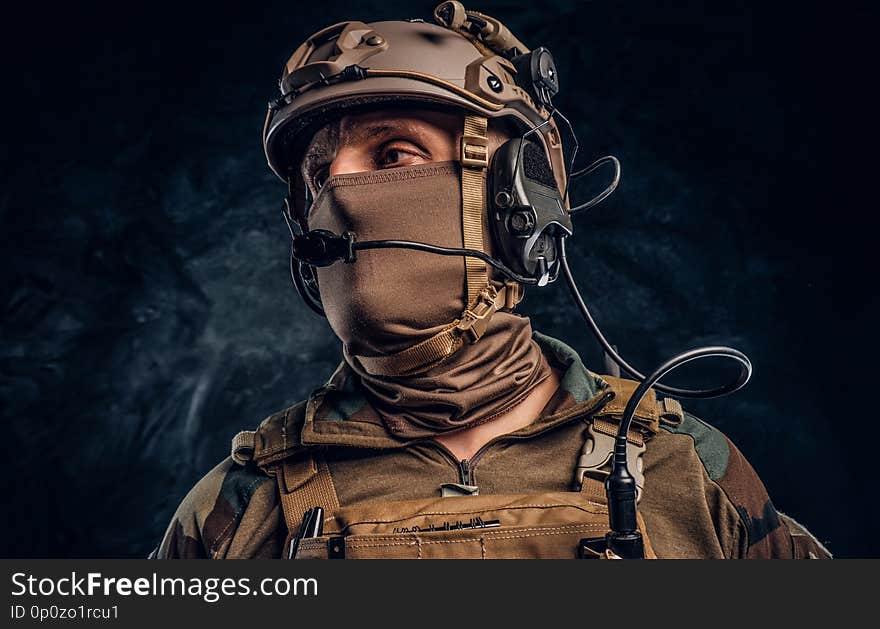 Close-up portrait. Private security service contractor in camouflage helmet with walkie-talkie. Studio photo against a dark textured wall