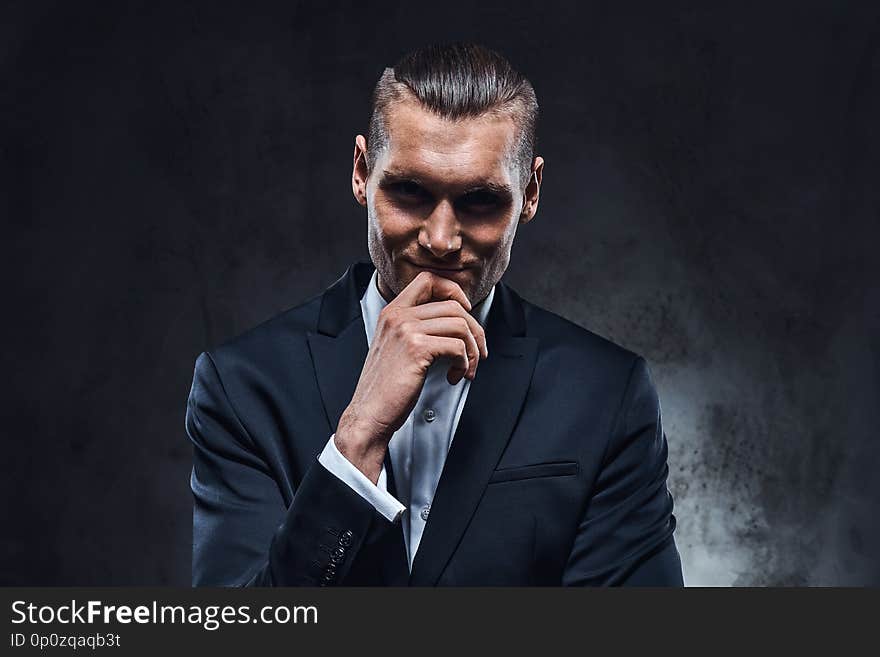 A confident businessman in black suit wearing elegant black suit. Studio shot on a dark textured wall