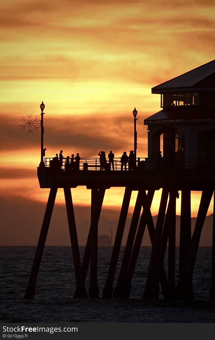 Silhouettes of people standing on the end of the Huntington Beach pier during a vibrant orange sunset over the ocean. Silhouettes of people standing on the end of the Huntington Beach pier during a vibrant orange sunset over the ocean