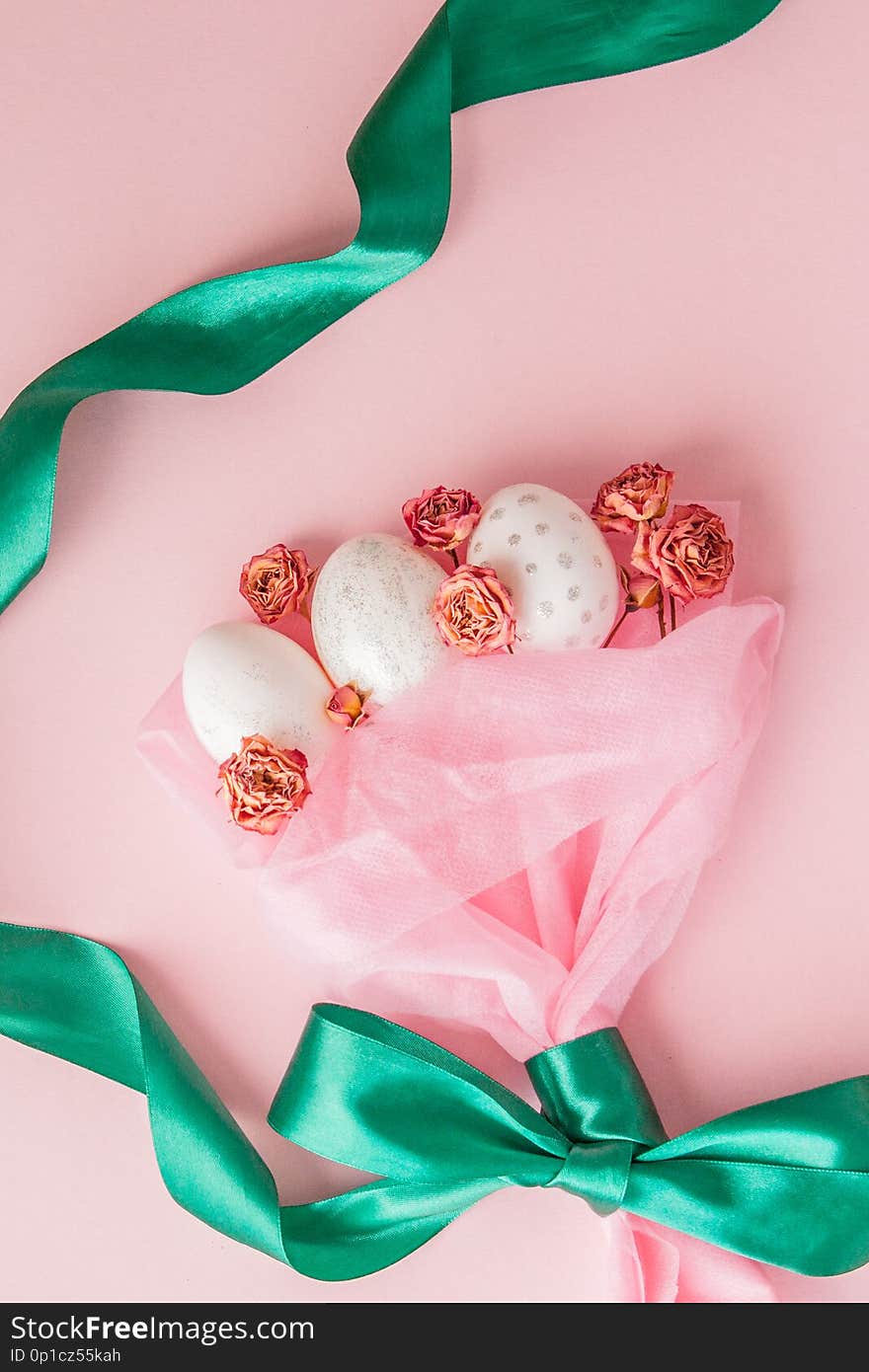 White Easter eggs in a bouquet with a green ribbon on pink background