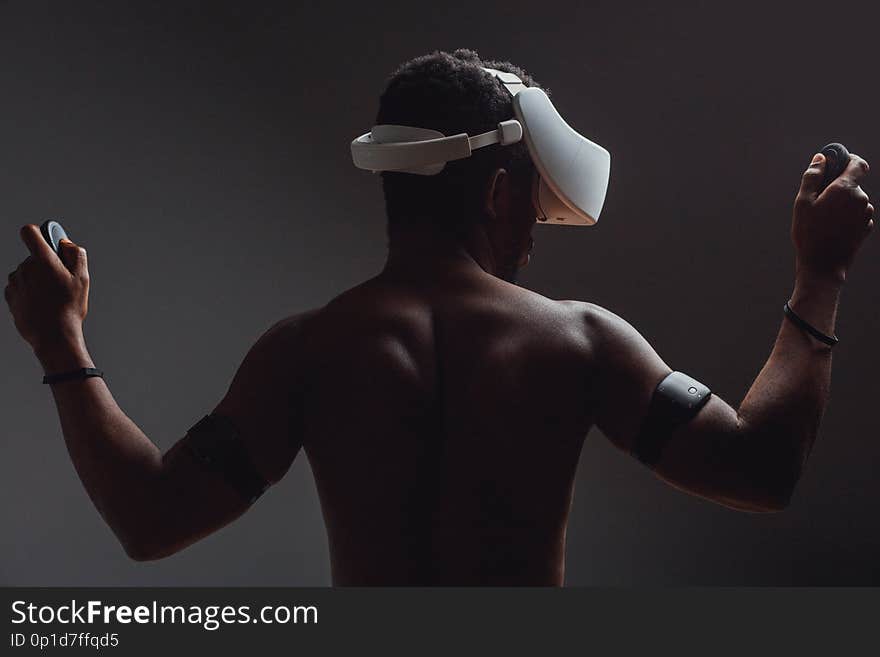 Backside of African male muscular athlet with naked torso using vr headset