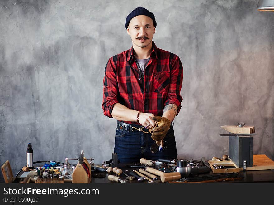 Attractive man is standing at the table and looking at the camera in the workshop. close up photo
