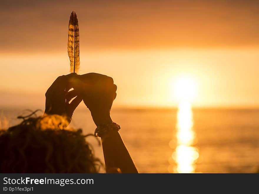 Woman hands taking a feather in front of an amazing golden and hot sunset over the sea. vacation and freedom independence concept