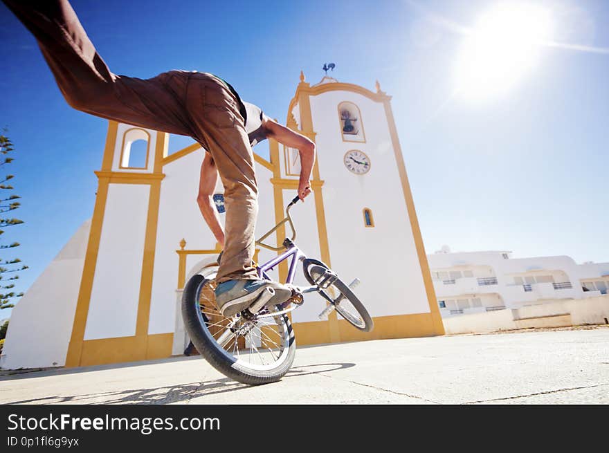 Young man have fun doing tricks with freestlye bike in a sware in front of a church. contrast between classic and modern related lifestyle. sunny day of summer