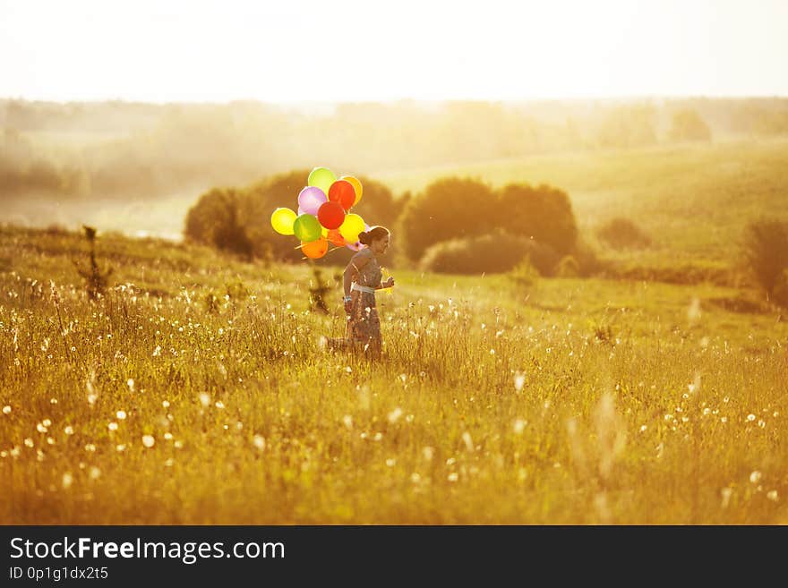 Young happy woman running across the field with balls