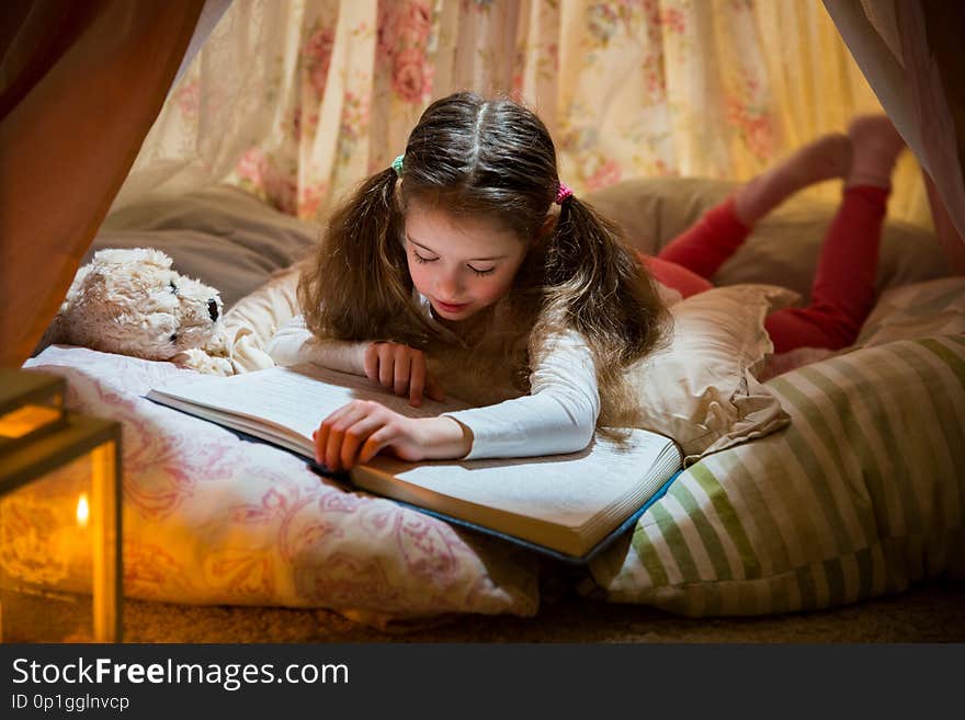 Cute little girl lying on pillows in homemade pink tent with flower