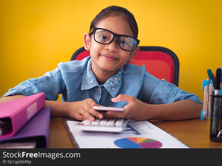 Cute girl smiling and holding a mobile phone on working desk yellow background, Education concept