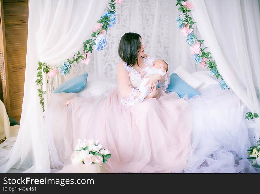 Young Mother In A Boudoir Dress With A Baby In Her Arms By The Canopy Bed