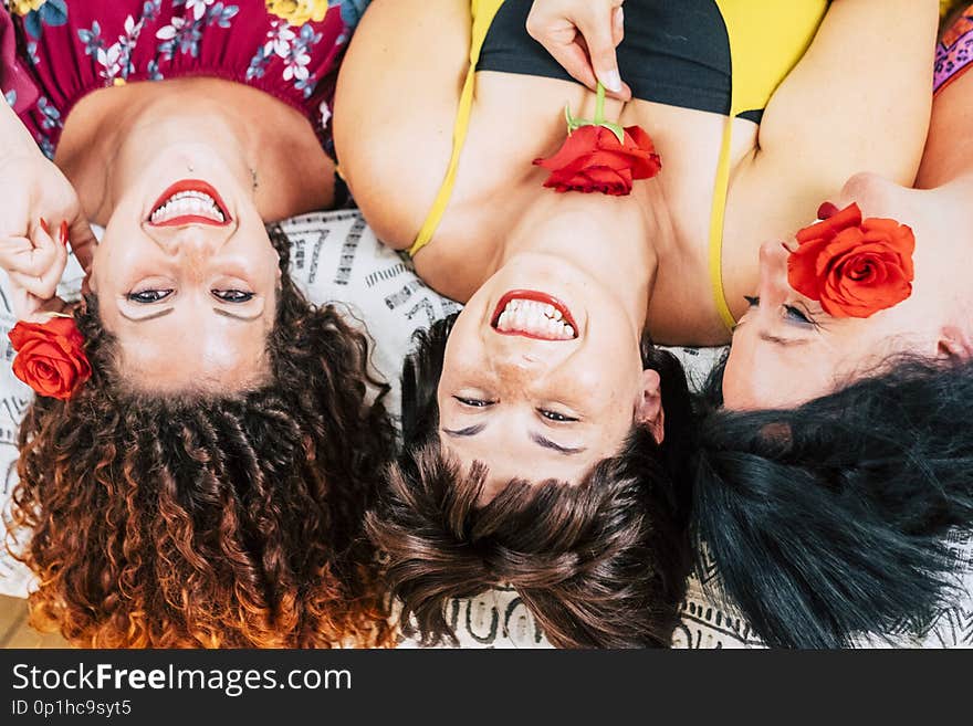 Playful group of young females friends at home together laughing and smiling. lay down on bed and taken from aerial view. make up beauty perfect to go out and rose for each one. beautyness concept
