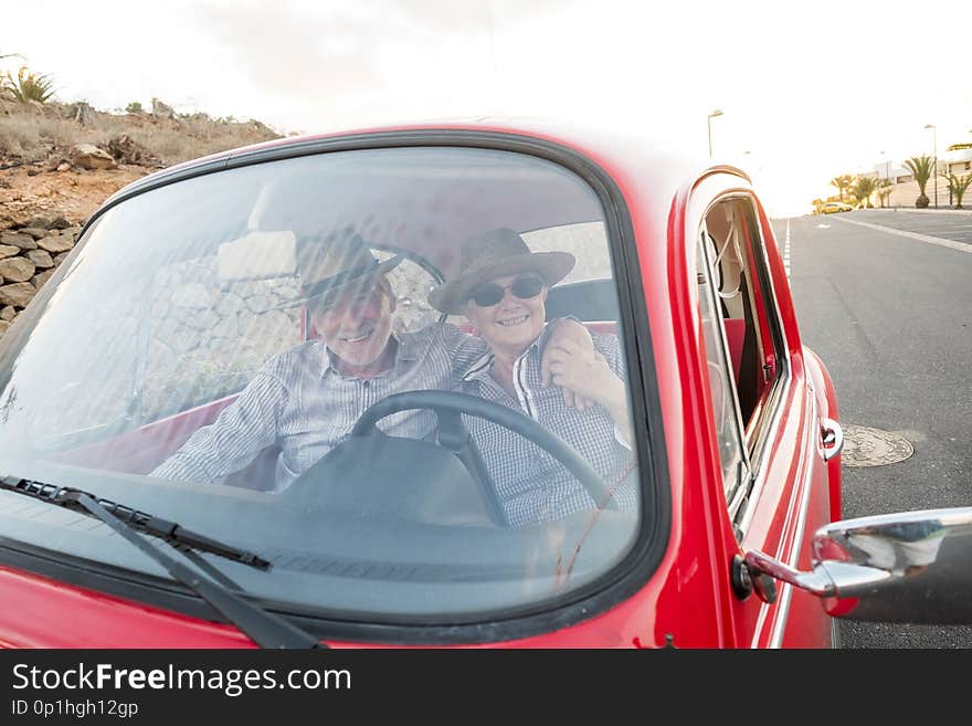 Nice adult couple hug and love inside a red old vintage car parked on the road. smiles and have fun traveling together. happiness