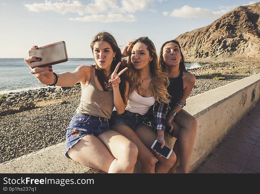 Group of three women in friendship taking selfies and using phone near the beach in Tenerife. Sunset time, lot of smile and happiness in vacation. Beautiful girls enjoy the indipendent life. Group of three women in friendship taking selfies and using phone near the beach in Tenerife. Sunset time, lot of smile and happiness in vacation. Beautiful girls enjoy the indipendent life