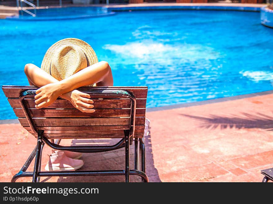 Tourist in hat lies on louger near swimming pool for relax summer vacation concept.