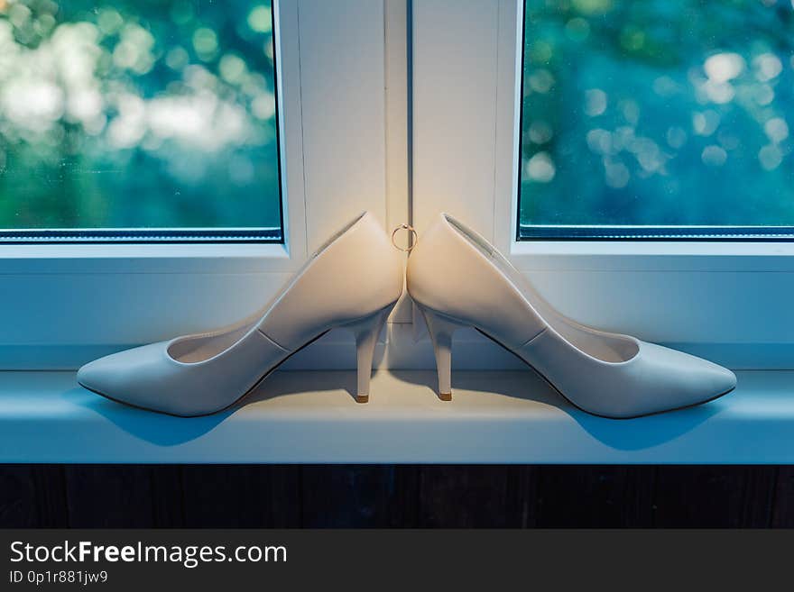 Women`s beautiful wedding shoes on the window with a wedding ring.