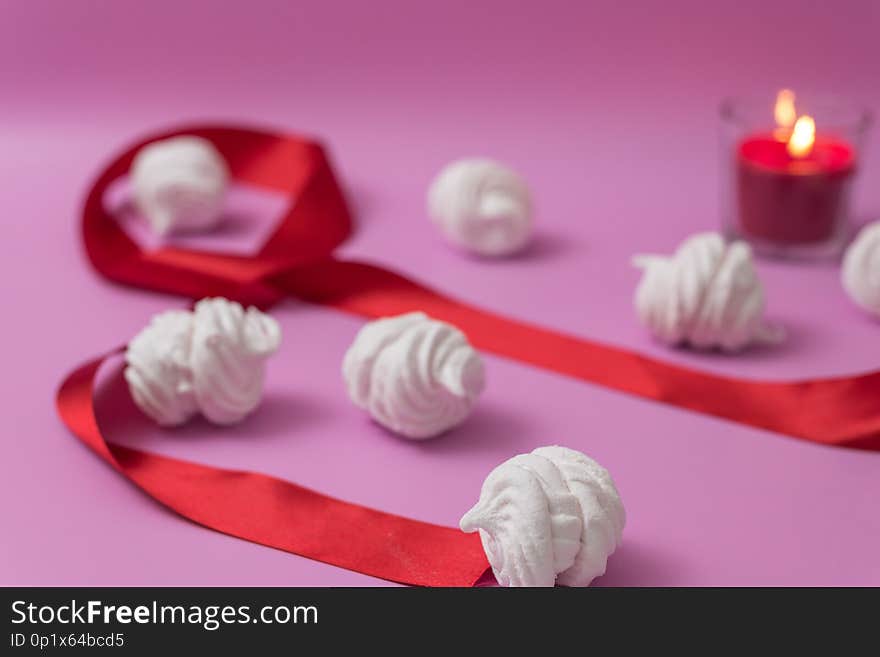 White homemade zefir or marshmallow on pink background with red candle