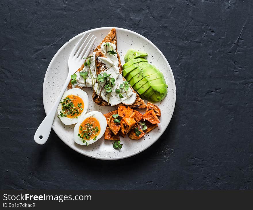 Cream cheese toast, avocado, boiled egg, baked sweet potatoes - delicious healthy breakfast or snack on a dark background, top view