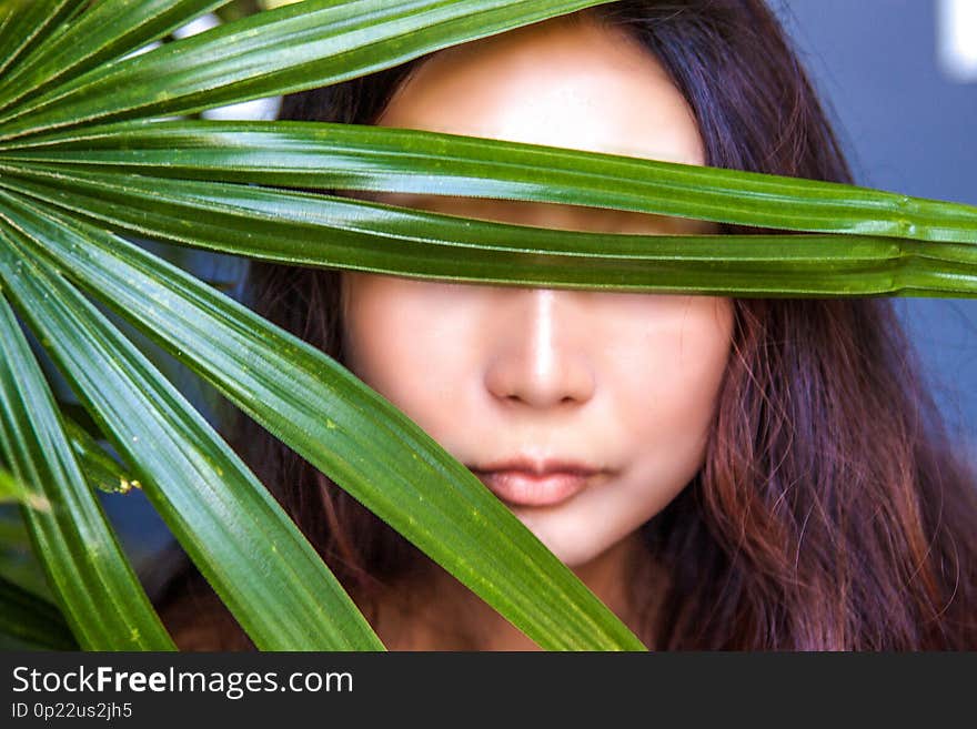 A beautiful woman is hiding behind palm leaves. Eastern beauty and skin care.