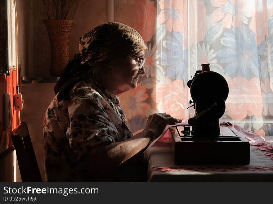 Senior woman in spectacles use sewing machine, silhouette of old dressmaker