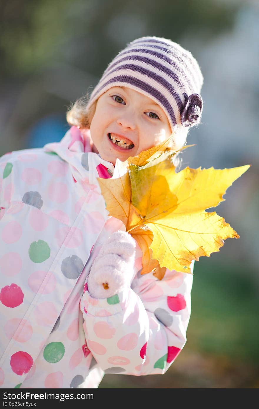 Young girl showing missing teeth. Holding yellow leafs in hand and posing. Spring sunny day. Young girl showing missing teeth. Holding yellow leafs in hand and posing. Spring sunny day