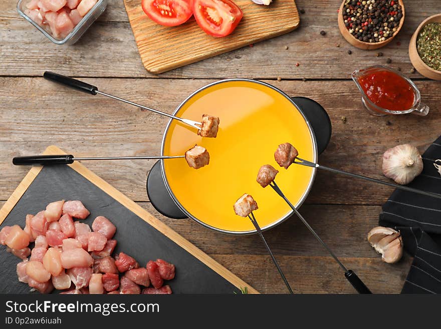 Flat lay composition with fondue pot and meat on wooden table