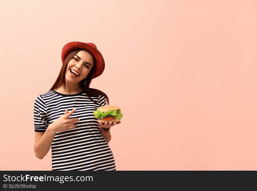 Young woman with tasty burger on color background. Space for text