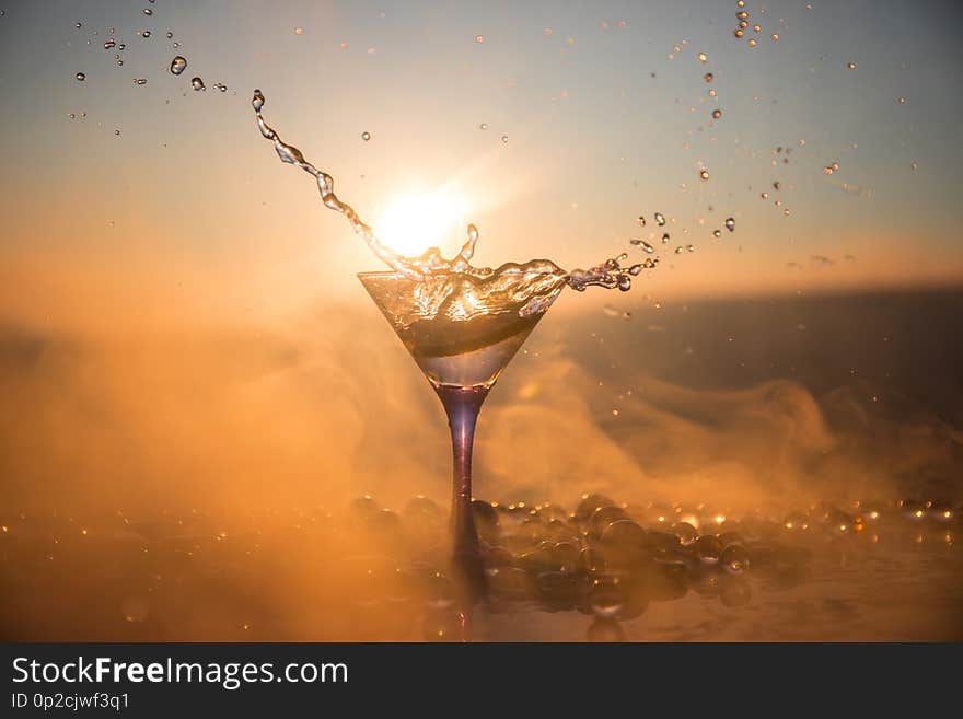 Martini cocktail glass in hand splashing on dark toned smoky background or colorful cocktail in glass with splashes and olives.