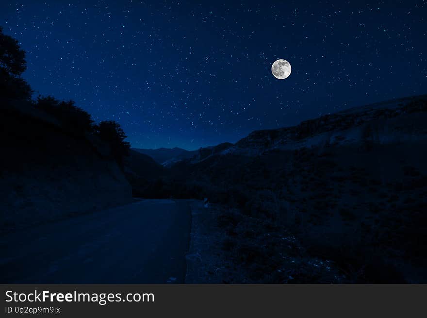 Mountain Road through the forest on a full moon night. Scenic night landscape of country road at night with large moon. Mountain Road through the forest on a full moon night. Scenic night landscape of country road at night with large moon