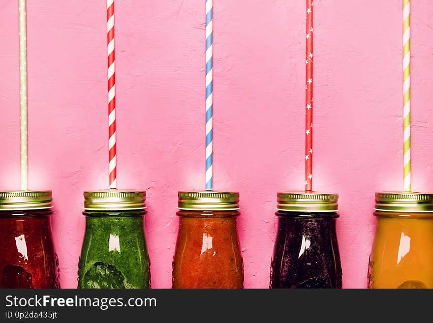 Multicolored detox vegan vegetable juices and smoothies in glass bottles on pink table, raw diet and clean food concept, drink