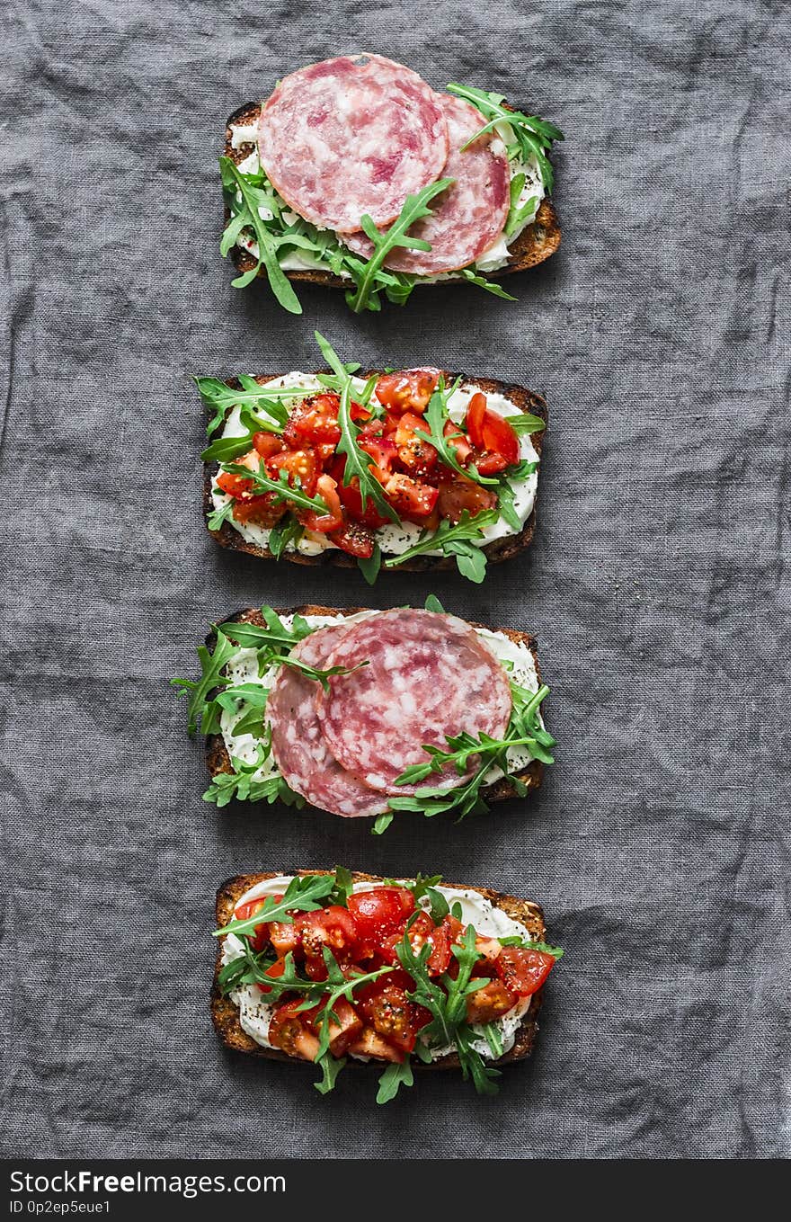 Tomatoes, italian sausage and rocket salad whole grain bread sandwiches on a gray background, top view. Copy space, flat lay. Delicious appetizers for wine, tapas