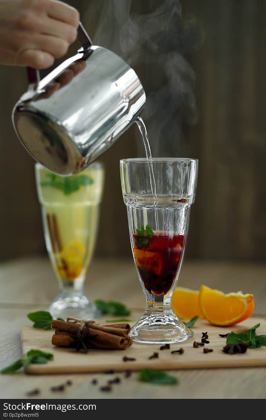 Pouring hot steaming water from steel pot in glass with vitamin drink. winter hot seasonal drinks.