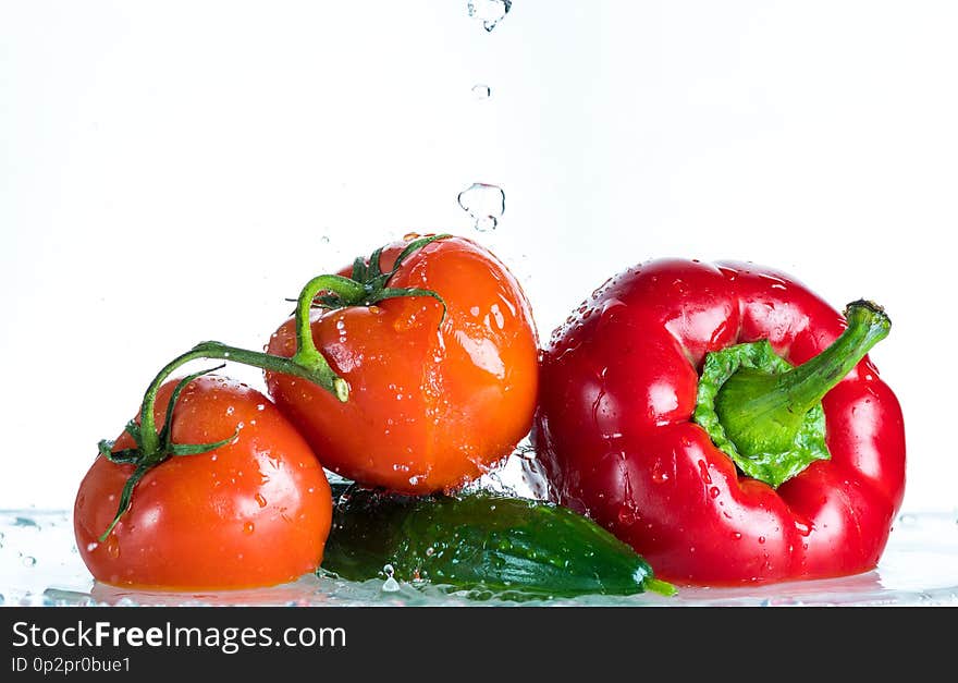 Fresh vegetables in a spray of water on a white background, tomato, cucumber, sweet pepper.