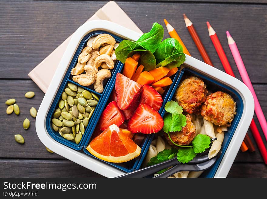 Lunch box for school. Healthy meal prep containers with beans meatballs, pasta, vegetables, berries, seeds and nuts in a container on a dark background, top view. Lunch box for school. Healthy meal prep containers with beans meatballs, pasta, vegetables, berries, seeds and nuts in a container on a dark background, top view