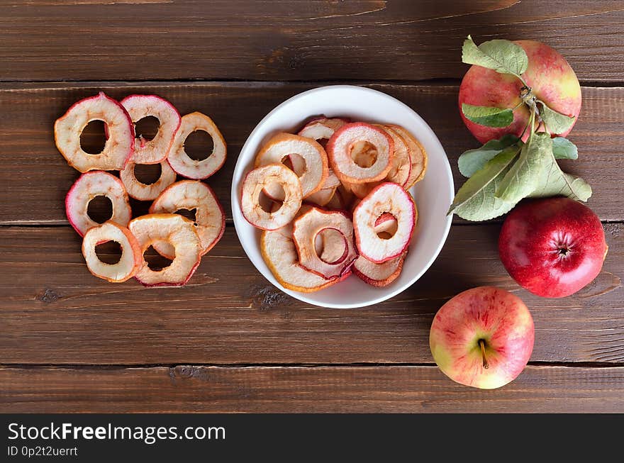 Dried apple rings in white bowl on a wooden table ahd fresh apples. Top view, flat lay