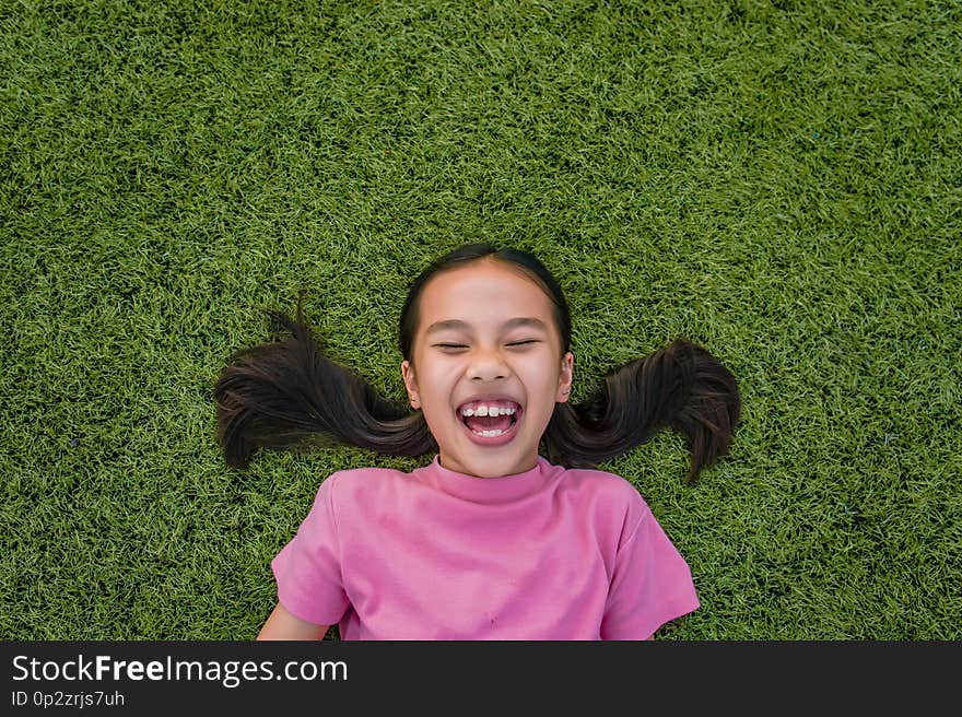 kid asian girl`s lie leisurely on the Lawn floor and smile looking at.