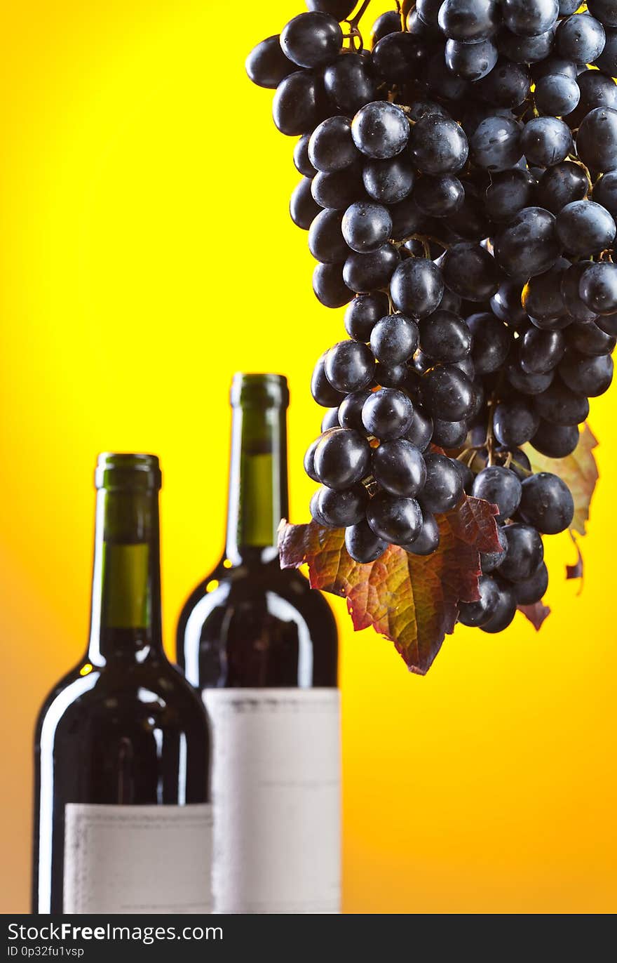 Grapes and bottles of red wine on yellow backgrond. Selective focus