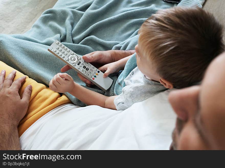 Father and toddler are watching television together and switching the new programme with a remote control