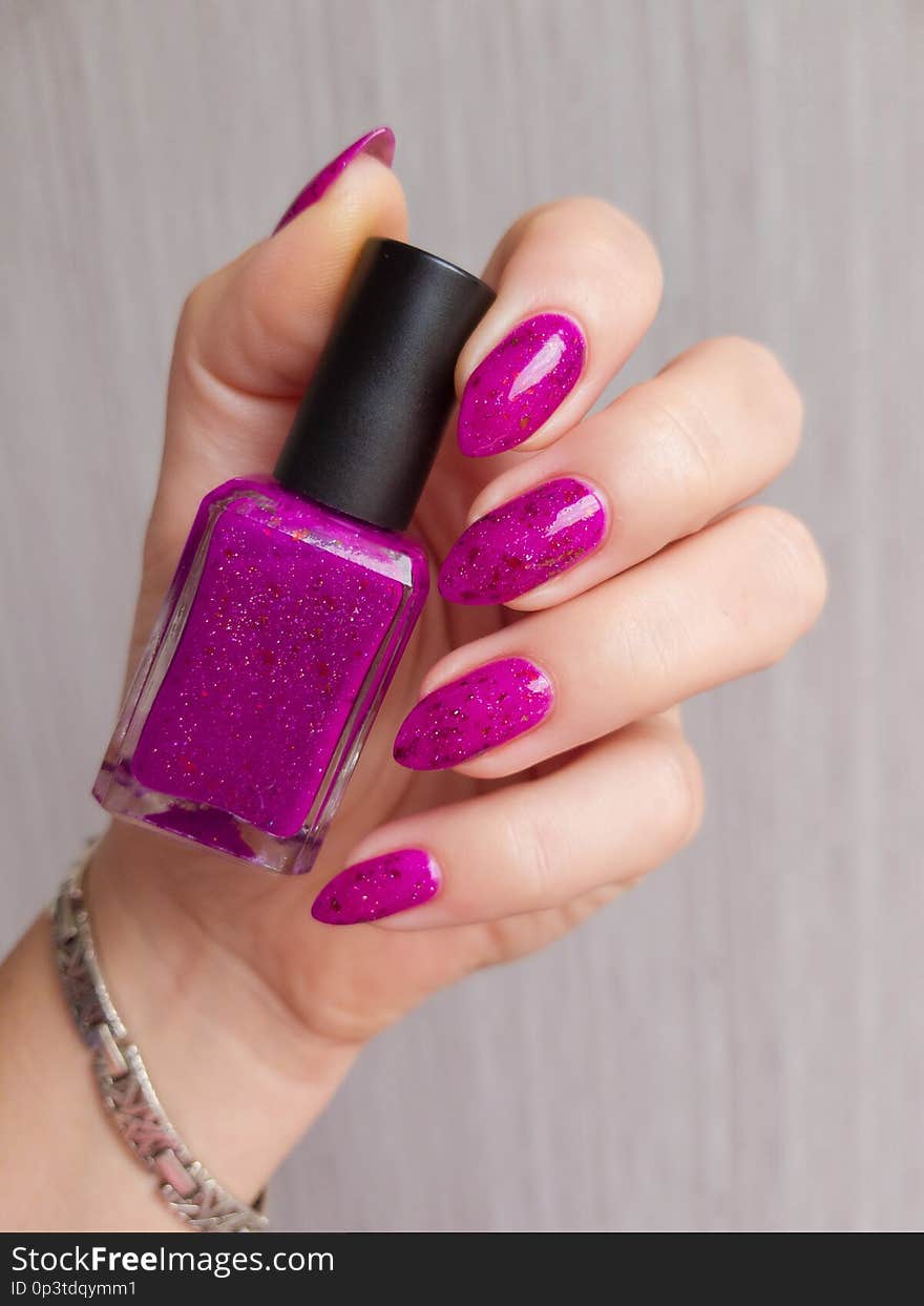 Female hands with long nails with red nail polish bottle