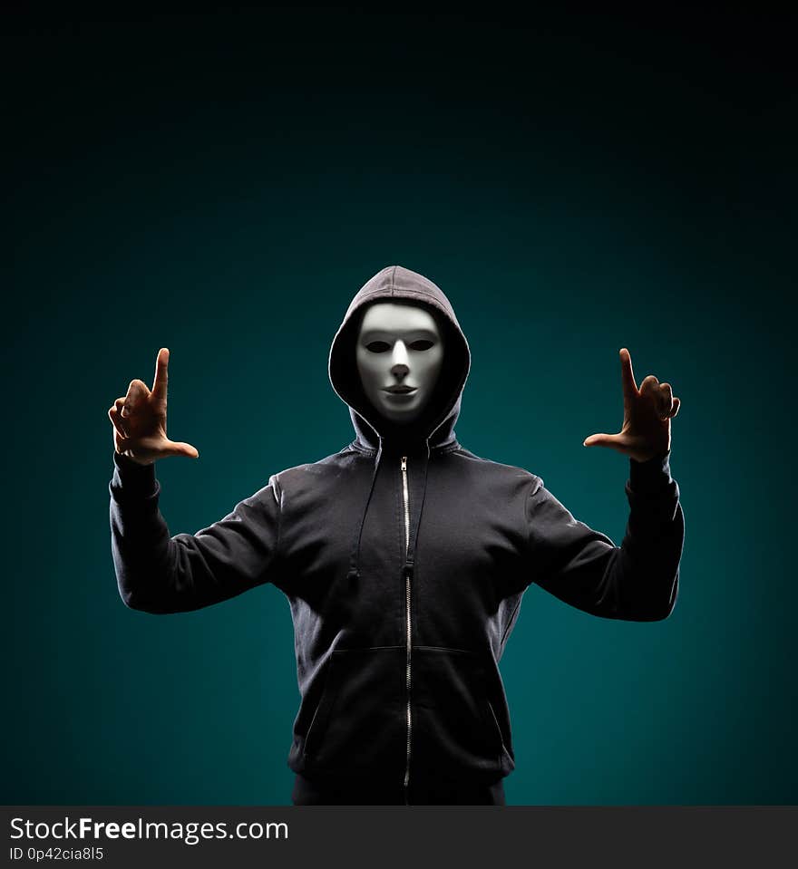 Portrait of computer hacker in white mask and hoodie. Obscured dark face. Data thief, internet fraud, darknet and cyber security concept.