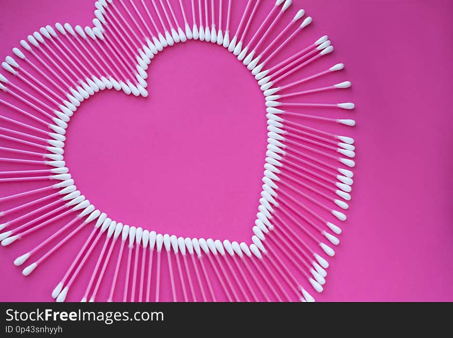 Cotton buds laid out in the shape of a heart on a pink background