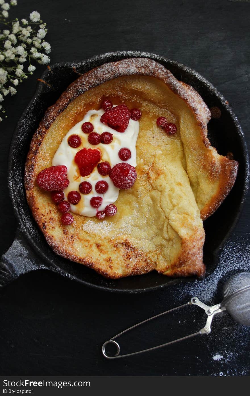 Dutch baby pancake on black background with red fruits and cream