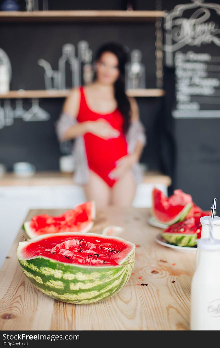 Halved bright watermelon on wooden table against unfocused pregnant woman.