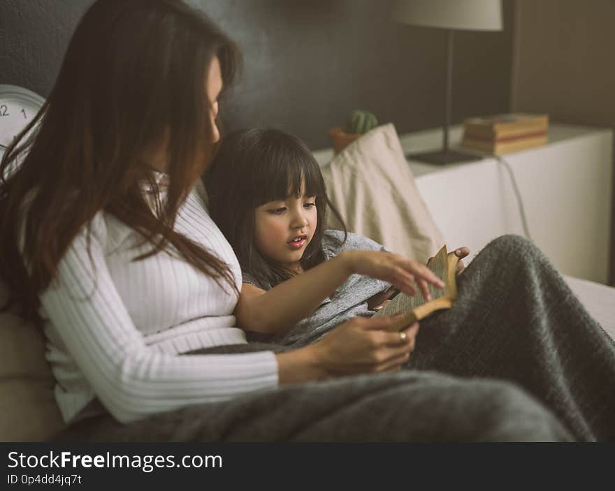 Mother and daughter reading book at home in the bedroom.