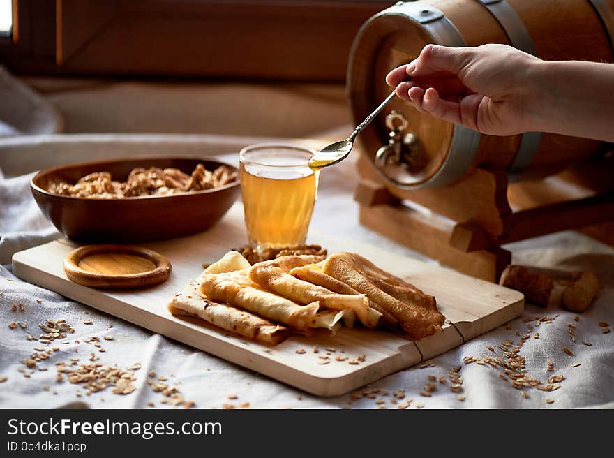 Mead and pancakes. Russian dish for Shrove Tuesday. Farewell to winter. The hand in the frame. Honey from a spoon dripping on pancakes. Mead and pancakes. Russian dish for Shrove Tuesday. Farewell to winter. The hand in the frame. Honey from a spoon dripping on pancakes