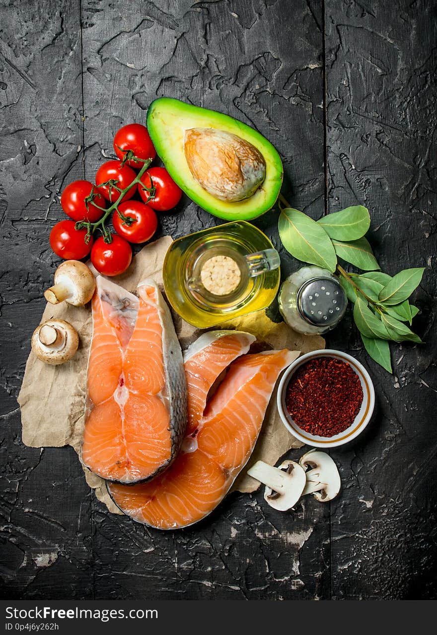 Healthy food. Salmon steaks with vegetables, herbs and spices. On a black rustic background