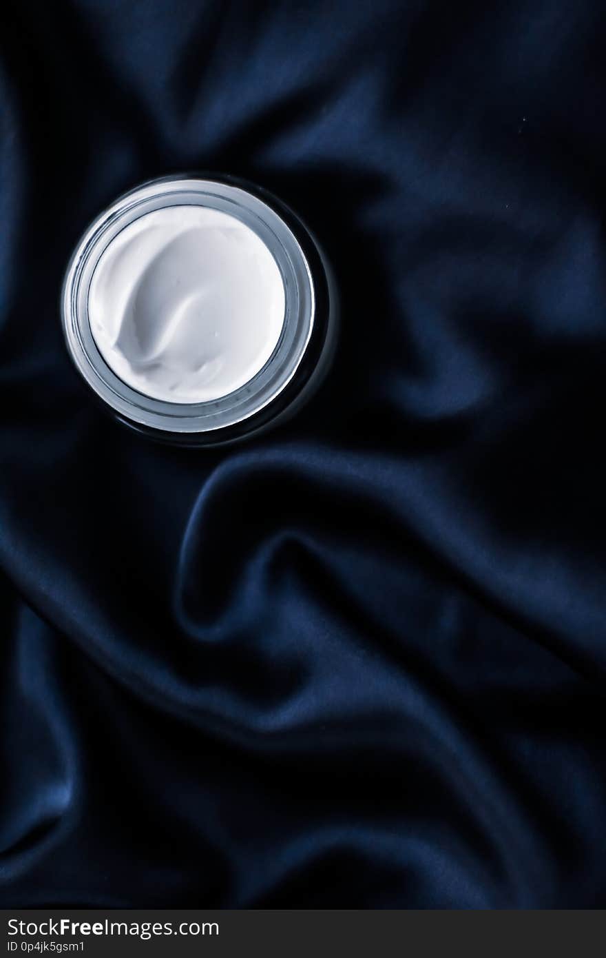 Luxury face cream jar on a dark blue silk