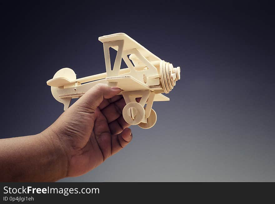 Cropped hand holding toy wooden retro airplane on dark background for travel concept
