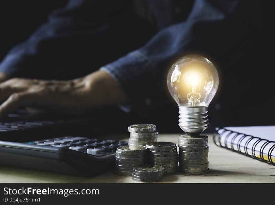 Man working with a light bulb on stack of coins for business and accounting concept.