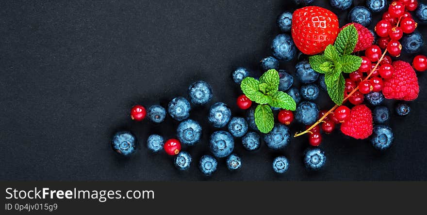 Berries mixed on a black background with copy space. Strawberry, Raspberry, Red currant, Blueberry and Blackberry, top view..