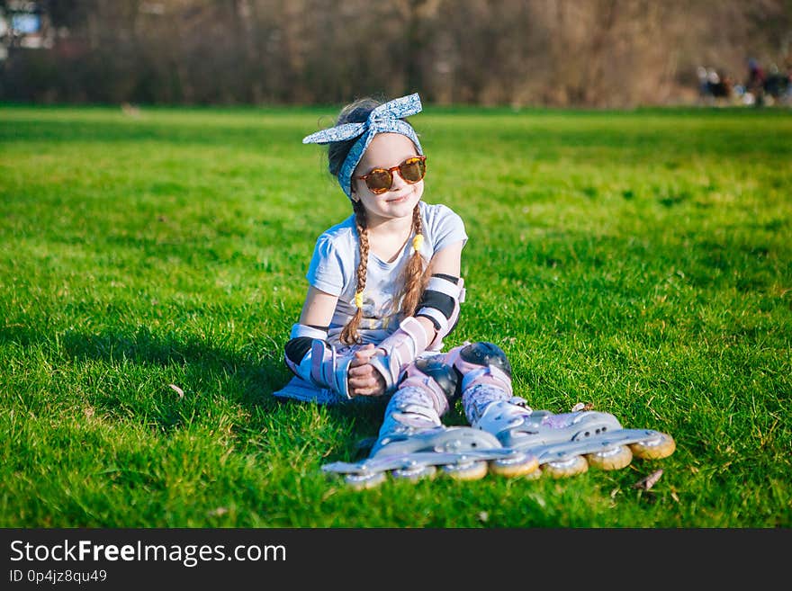 Cute curly girl enjoys sitting in roller skates and sunglasses and looking at the camera on beautiful sunny day. Cute curly girl enjoys sitting in roller skates and sunglasses and looking at the camera on beautiful sunny day
