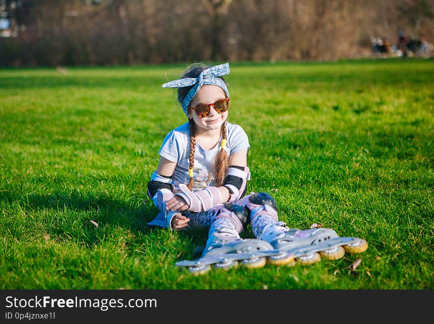 Cute curly girl enjoys sitting in roller skates and sunglasses and looking at the camera on beautiful sunny day. Cute curly girl enjoys sitting in roller skates and sunglasses and looking at the camera on beautiful sunny day